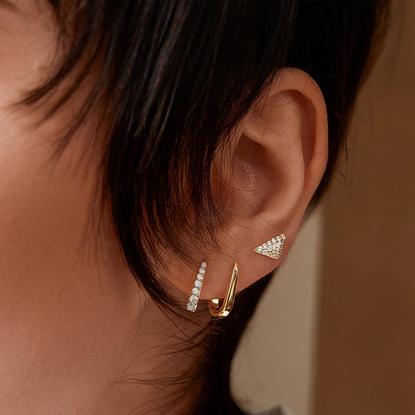 Close-up of an ear wearing gold and diamond earrings against a neutral background